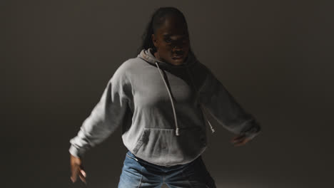 Studio-Portrait-Shot-Of-Young-Woman-Wearing-Hoodie-Dancing-With-Low-Key-Lighting-Against-Grey-Background-10